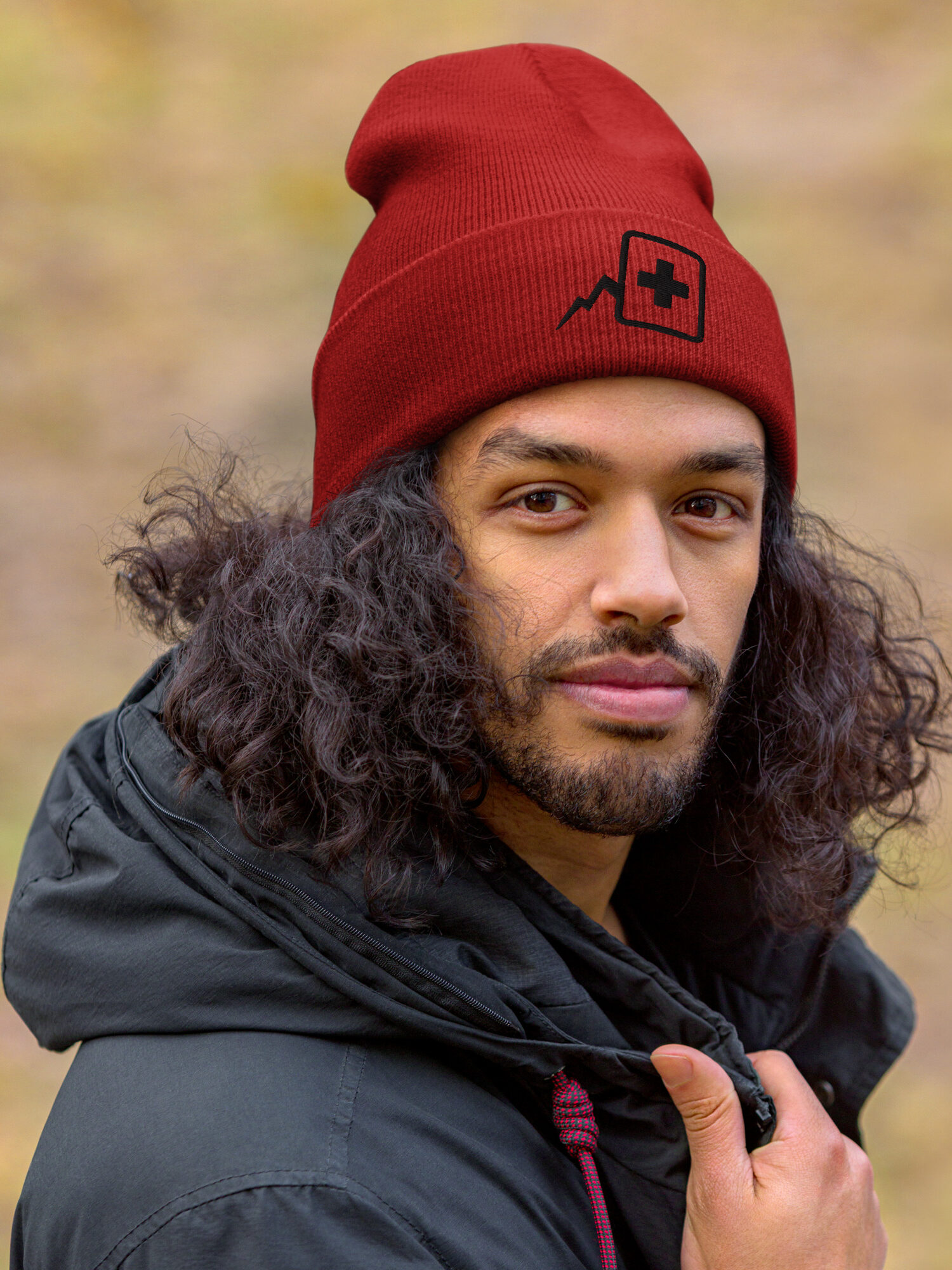 Homme bronzé avec cheveux long bouclé avec un manteau gris foncé portant un bonnet avec le logo "Atelier du Deck"