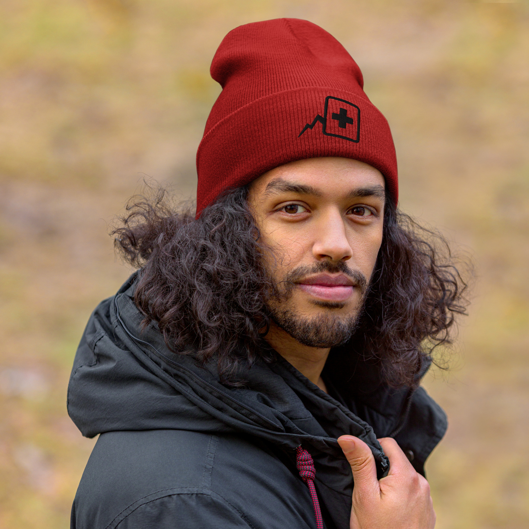 Homme bronzé avec cheveux long bouclé avec un manteau gris foncé portant un bonnet avec le logo "Atelier du Deck"